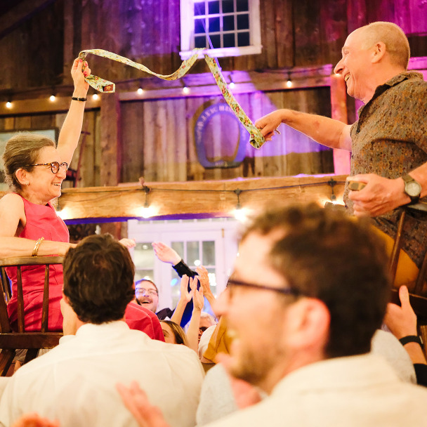 Tim and Di up in chairs doing the Hora, both beaming. In the background you can see Aaron mid-cheer, jumping for joy.