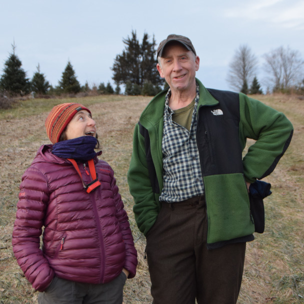 Tim and Di standing in a field, Tim is looking at the camera with a wry expression while Di looks affectionately up at him.
