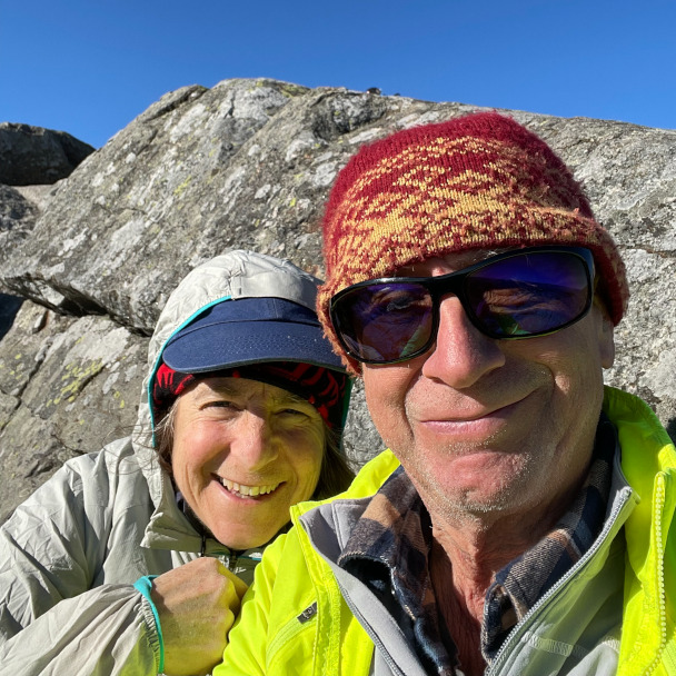 A selfie of Tim and Di smiling on a rock, probably on some big ole mountain somewhere. Tim is wearing his sunglasses which he loves to wear and hide his eyes in photos CONSTANTLY.