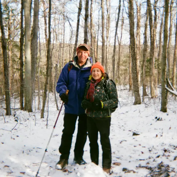 Tim and Di next to each other in their full winter gear on a snowy hiking trail.
