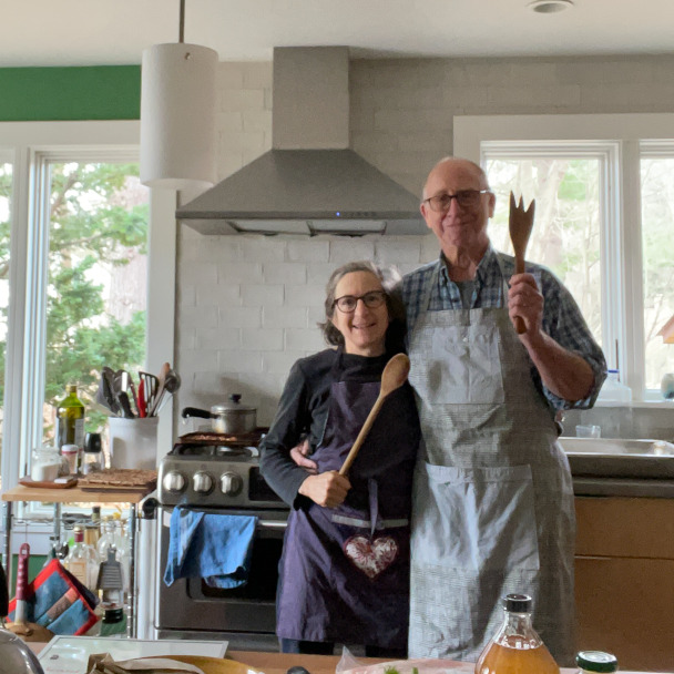 A cute pic of Tim and Di in the kitchen, both wearing aprons and wielding large wooden spoons with goofy grins on their face.