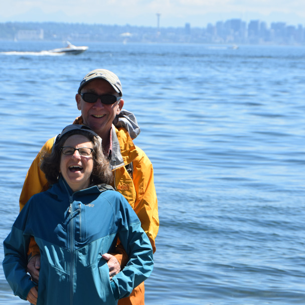 Tim and Di standing in front of the Seattle skyline, they're both laughing with a twinkle in their eye.